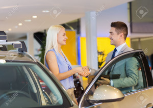 auto business, car sale, consumerism, gesture and people concept - happy woman with car dealer making deal and shaking hands in auto show or salon